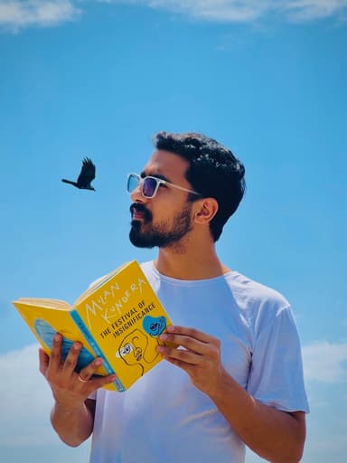 Karan Kapoor reading a Milan Kundera book under a blue sky